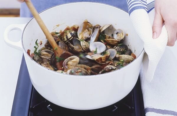 Clams being stirred in white pot over hob