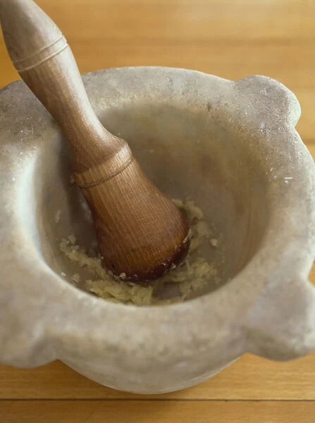 Crushed garlic in stone mortar bowl with wooden pestle, close-up, high angle view