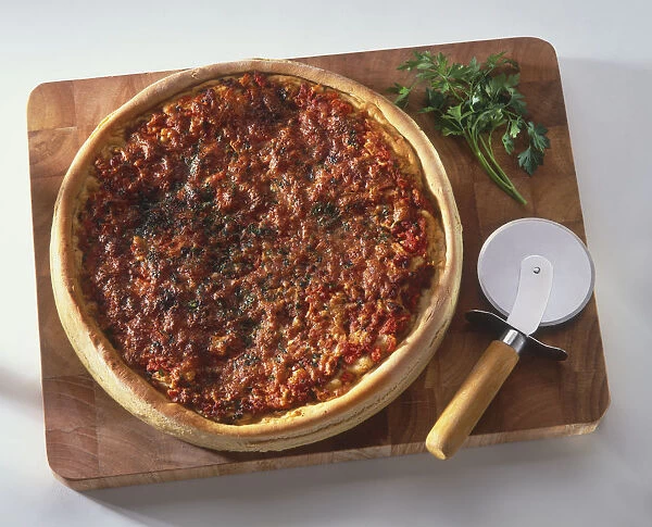 Deep-dish pizza from Chicago, on chopping board with pizza cutter and herbs, view from above