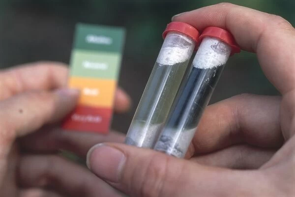 Hand holding two plastic test tubes containing soil, matching them against a pH colour chart