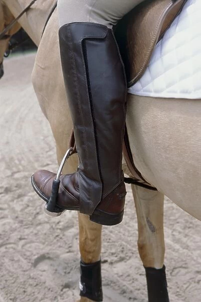 Person sitting on palomino horse wearing brown leather riding boots with foot in stirrup, close-up