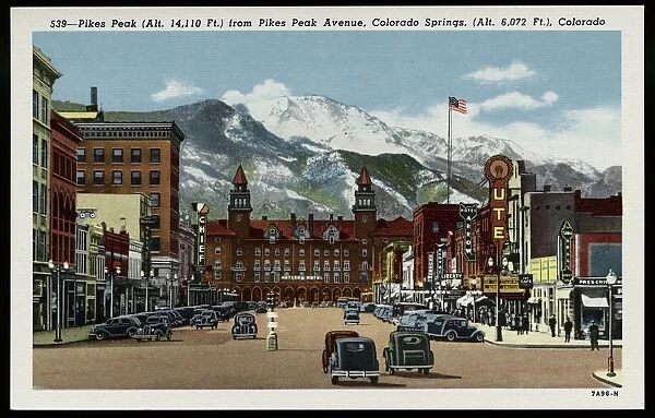 Pikes Peak Avenue. ca. 1937, Colorado Springs, Colorado, USA, 539-Pikes Peak (Alt. 14, 110 Ft. ) from Pikes Peak Avenue, Colorado Springs, (Alt. 6, 072 Ft. ), Colorado. Pikes Peak Avenue is a broad and stately street pointing directly toward the Peak from which it is named that looms above it. At the west it terminates at the Antlers Hotel whose graceful towers form a perfect sight like those on a rifle for the view of Pikes Peak. In the summer season it is thronged with visitors of every station in life from every state and country, for the Avenue is the center of tourist activity. Few who have traversed its broad pavements will forget it as it is one of the most impressive street spectacles in the world