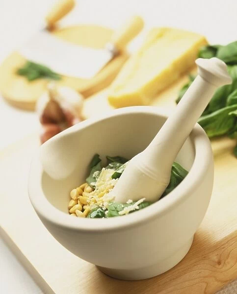 Pine nuts, grated parmesan cheese and green basil leaves in stone pestle with mortar, elevated view