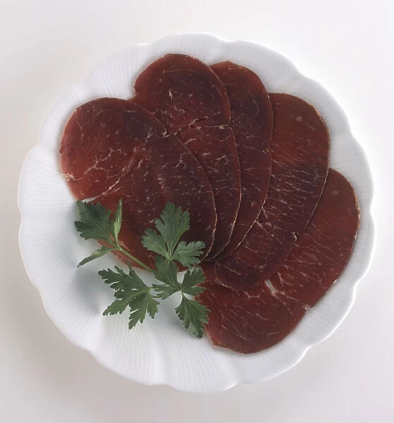 Plate of Bresaola, slices of cured raw beef garnished with herb, a typical dish from Lombardy, Italy, view from above