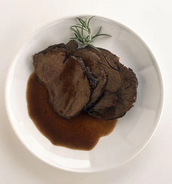 Plate of Manzo al Barolo, slices of marinated beef in red wine sauce, garnished with sprig of rosemary, a typical dish from Piedmont, Italy, view from above