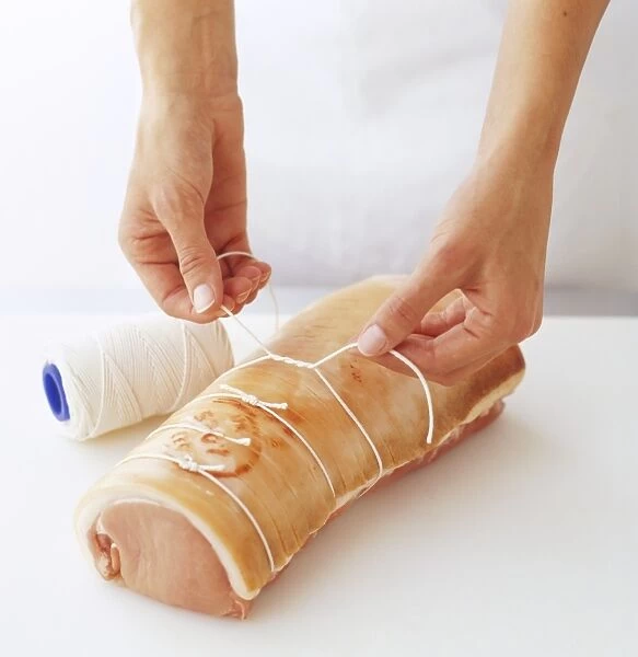 Pork loin rolled into a loaf shape being tied with kitchen string