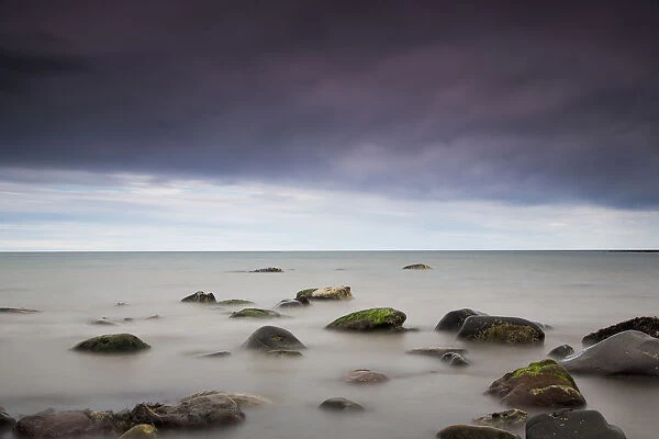 Rocks in tranquil water under storm clouds; Northumberland england