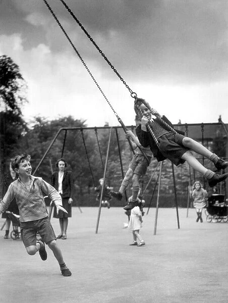 Two boys playing on swings in the playground. 10th July 1942