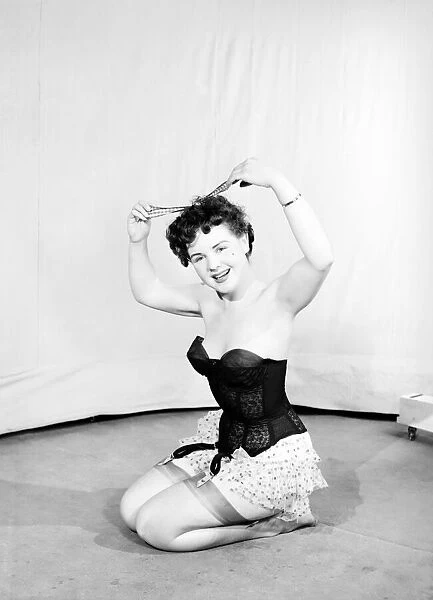 Clothing: Fashion: Underwear: Woman wearing corsett placing bow in hair. 1959