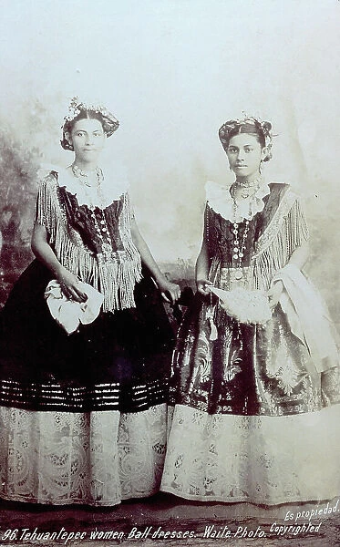 Full-length portrait of two Mexican girls in rich party dresses. The dresses are rather complicated because elements of traditional Mexican dress have been combined with western styles
