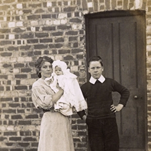 Girl and boy with baby and spaniel outside a house