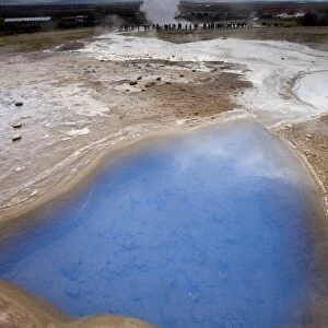 Blue water in geothermal pool with stream from Strokkur Geysir visible in the distance