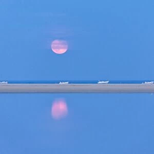 The pink full moon is reflected in the blue water of the Notteri pond, Villasimius