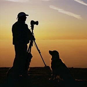 A photographer and dogs on Black Combe at sunset with the Isle of Man behind in the Lake District UK