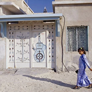 UAE, Dubai, Bur Dubai Young girl passing building with carved and decorated doorway