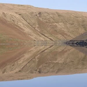Banks of reservoir reflected in water, Claerwen Dam, Elan Valley, Powys, Wales, january