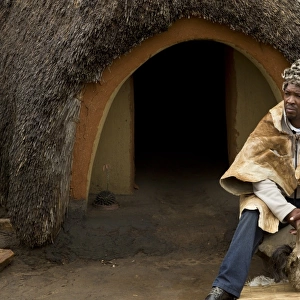 Inyanga herbal healer sitting outside hut in traditional Basutho village, Lesotho, November