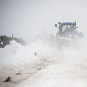 New Holland tractor clearing snow off rural road after snowstorm, Cumbria, England, March