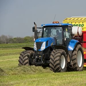 New Holland tractor with Pottinger forage wagon, picking up grass in silage field, Northumberland, England, May