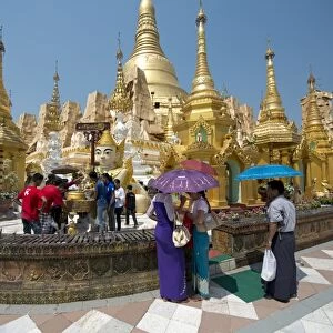 People with umbrellas at Buddhist gilded pagoda and stupa, Shwedagon Pagoda, Yangon, Myanmar, March
