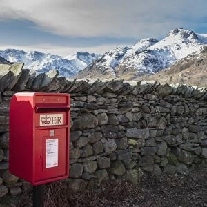 Royal Mail postbox beside drystone wall, with snow covered fell in background, Chapel Stile, Langdale