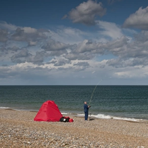 Sea angler fishing beside shelter on shingle beach, Cley, Norfolk, England, september