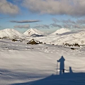 Shadow of man and dog looking towards snow covered mountain peaks, viewed from Dubh Bheinn, Paps of Jura, Isle of Jura