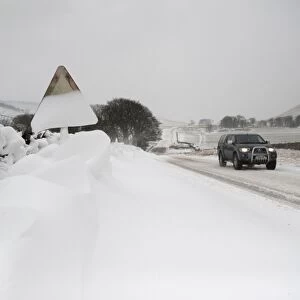 Snow covered roadsign and vehicle travelling along rural road after snowstorm, Cumbria, England, March