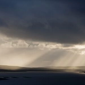 Stormy evening sky with sunbeams over coastline, looking towards Yell, Fetlar, Shetland Islands, Scotland, June