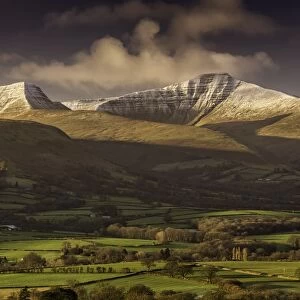 View of farmland and snow covered hills at sunrise, Penyfan and Corn Du, Brecon Beacons N. P