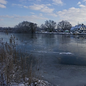View of frozen river and pub on riverbank, The Ferry House, River Yare, The Broads, Surlingham, Norfolk, England