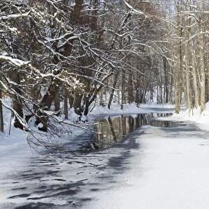 View of partially frozen river in snow covered forest habitat, Angelsberg, Vastmanland, Sweden, february