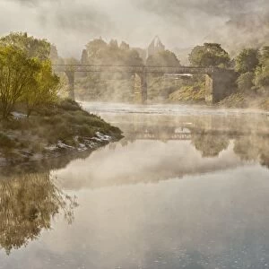 View of river, bridge and Cistercian abbey ruins in mist at dawn, Tintern Abbey, Tintern, River Wye, Wye Valley