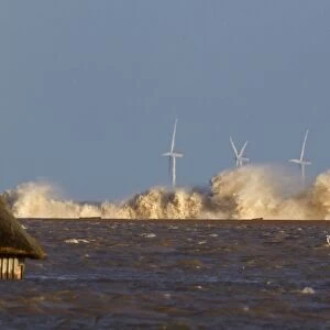 Waves crashing against remains of shingle sea defences, with flooded marshes
