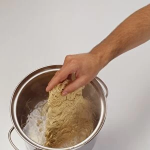 Block of dry noodles being lowered into a pot of boiling water, elevated view