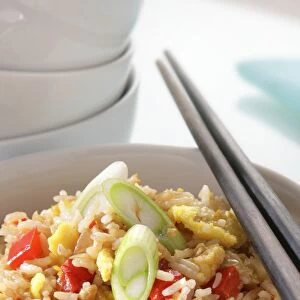 Bowl of egg-fried rice with red bell peppers and celery, with chopsticks resting on top, and a stack of bowls nearby, close-up