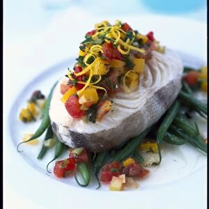 Close-up of a cod steak with brightly coloured tomatoes, peppers, garnished with lemon zest and chopped parsley and served on french beans