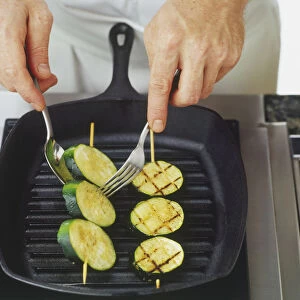 Courgette skewers cooking on char-gril being flipped over with spoon and fork