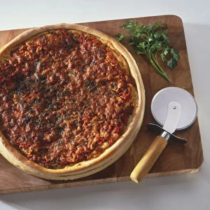 Deep-dish pizza from Chicago, on chopping board with pizza cutter and herbs, view from above