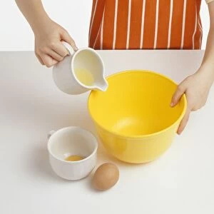 Girl pouring egg white into mixing bowl, cup containing egg yolk nearby