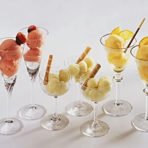 Glasses containing round balls of ice-cream, decorated with fruit and biscuits