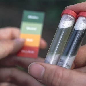 Hand holding two plastic test tubes containing soil, matching them against a pH colour chart