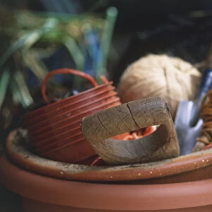 Large terracota pot containing stacked plastic pots, spade, trowel and spools of string, close up