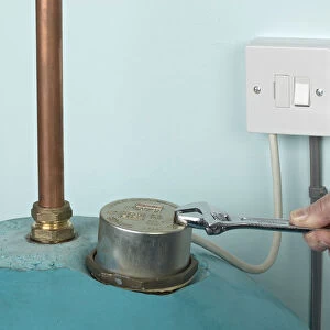 Man using adjustable spanner to remove nut on boiler cover, plug switched off, close-up