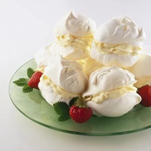 Meringues filled with cream, stacked in pile and served with fresh strawberries, presented on green dish