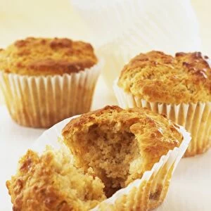 Three muffins in paper cases, muffin in forefront split open, revealing golden mixture