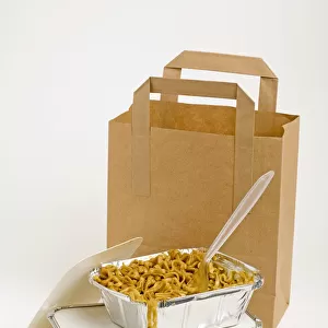 Noodles with plastic fork in aluminium container, on top of another container, and a paper carrier bag