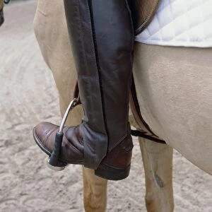 Person sitting on palomino horse wearing brown leather riding boots with foot in stirrup, close-up