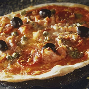 Pizza Capricciosa, round pizza with light crispy crust, topped with olives, ham, salami, capers and tomato sauce