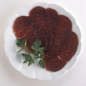 Plate of Bresaola, slices of cured raw beef garnished with herb, a typical dish from Lombardy, Italy, view from above